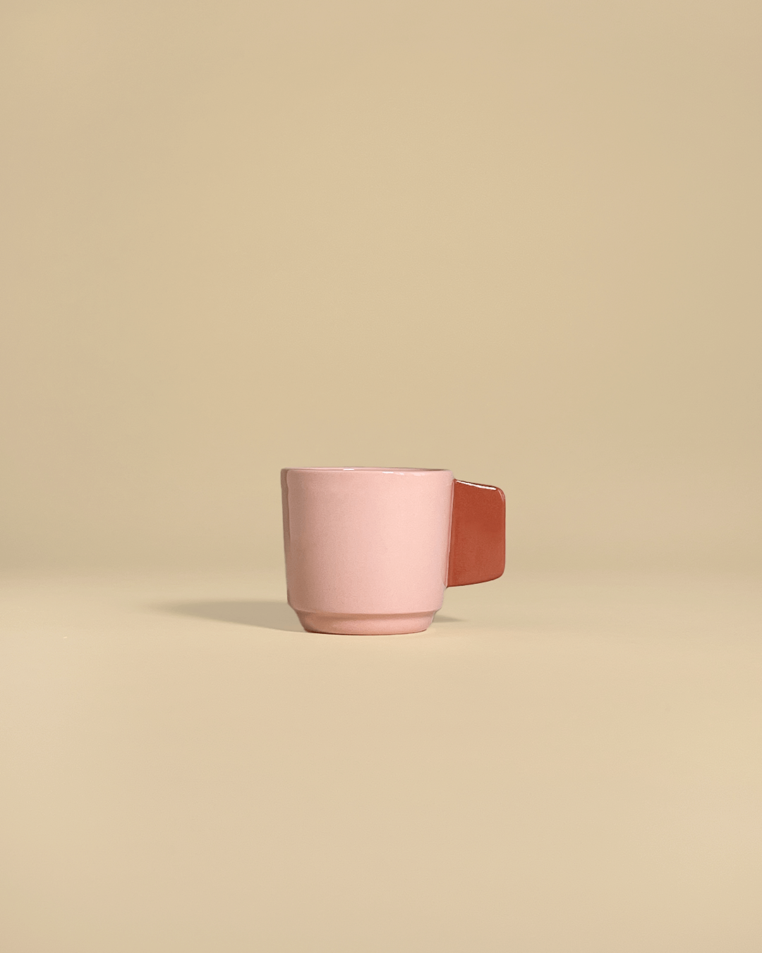 A ceramic espresso cup in a powdery pink with a terracotta colored handle.