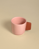 A ceramic espresso cup in a powdery pink with a terracotta colored handle.