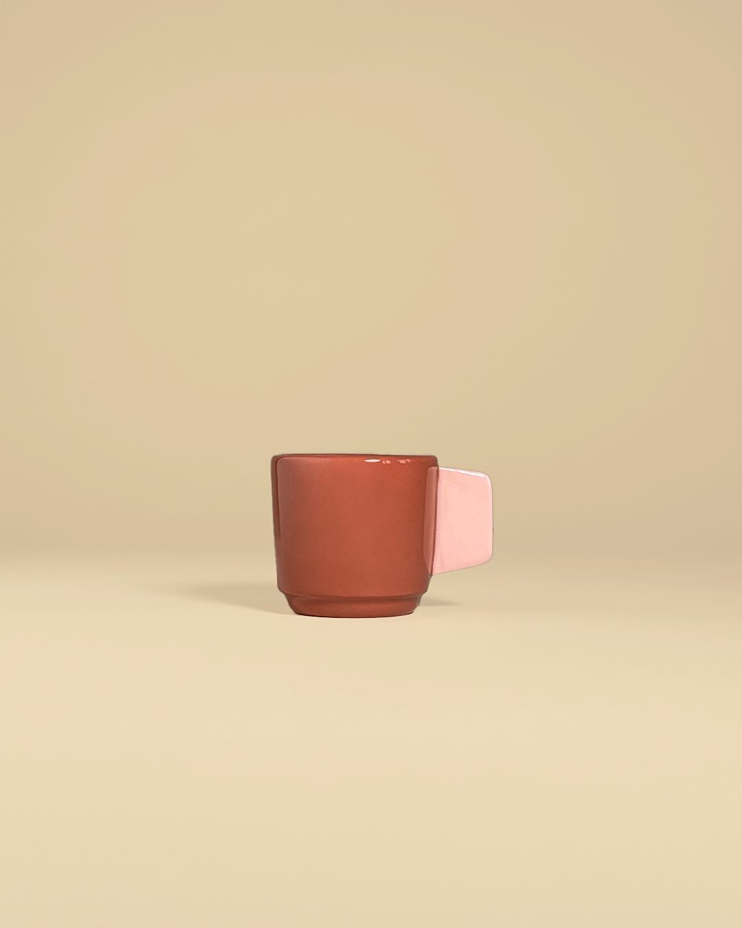 A ceramic espresso cup in terracotta and with a handle colored in powdery pink.