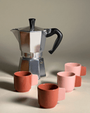 A Coffee Maschine and the ceramic espresso cups in terracotta and with a handle colored in powdery pink and vise versa.